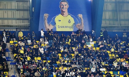 Al Nassr fans sit under a giant billboard of Cristiano Ronaldo