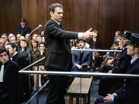 Defendant in court holding arm outstretched with his hand in a pistol shape.