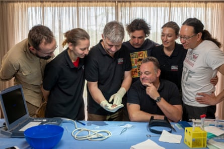 A group of people gather around a desk to look at a rhino embryo held in the palm of Thomas Hildebrandt, the BioRescue project head