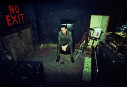 Ron sweats from inside his men’s threadbare suit after a show, in a rundown dressing room on a tour in the middle of America, 1996, with musical equipment, a suitcase, and a No Exit sign