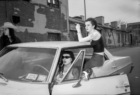 A black and white image of two women in Brooklyn smoking while hanging out of an old car, in front of derelict buildings during a break in shooting