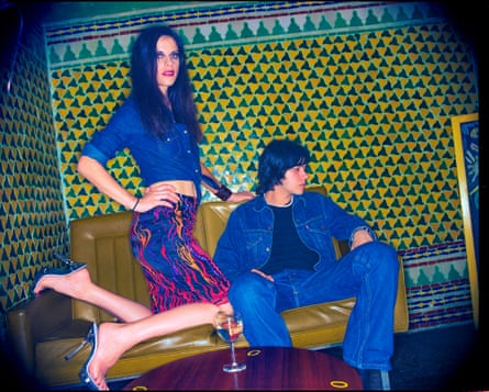 Cristina Martinez from Boss Hog (left), with Ali’s assistant, Aurelio Valle (singer of Calla) on a tan leather couch at a restaurant with psychedelic walls