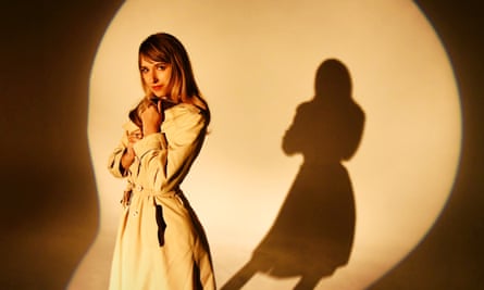 Musician Molly Lewis poses in a white coat in front of a front lit backdrop