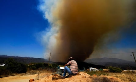 huge plume of smoke in the sky with man in foreground sitting on bare earth looking at it
