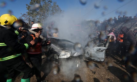Firefighters attempt to put out a blaze in a car with crowds watching