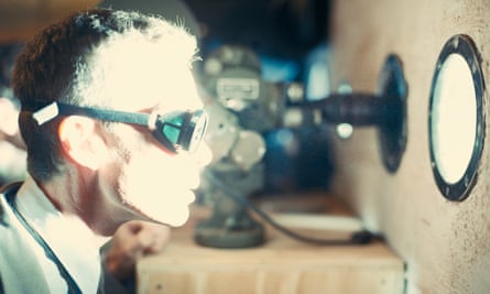 film still of a man wearing goggles lit by a very bright light