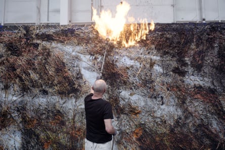 German painter Anselm Kiefer with a blowtorch burning off brushwood from one of his large paintings, in a still from Wenders’s 2023 documentary about him, Anselm