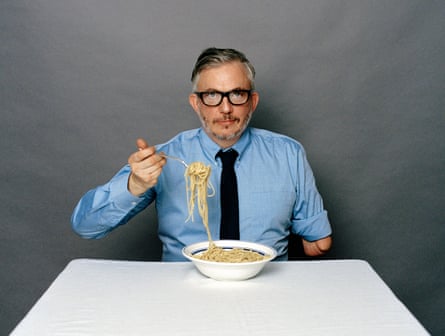 Self-portrait by Giles Duley in a shirt and tie, eating spaghetti.