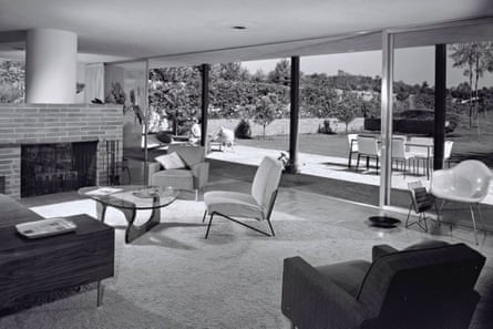 A black-and-white photo of a one-story ranch-style home with floor-to-ceiling plate glass windows looking onto a yard.