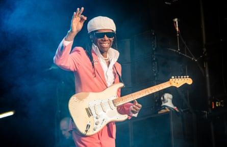 Rodgers in a pink suit, smiling, with a beat-up old Stratocaster