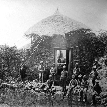 A period photograph showing several soldiers around a stone building with a grass roof