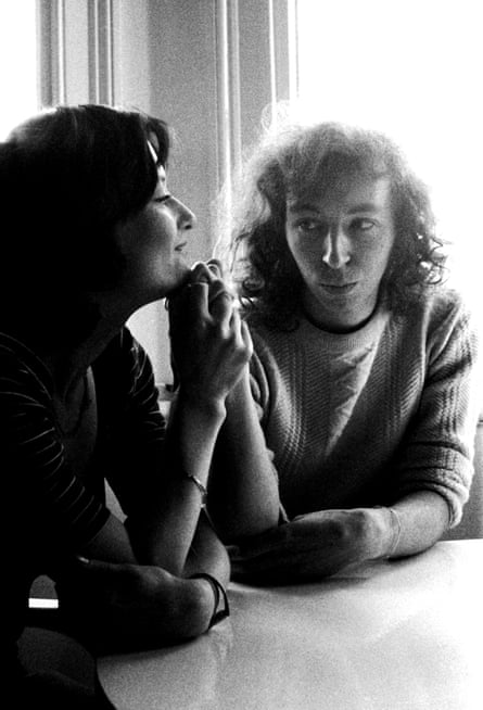 Black and white portrait of the Thompsons, sitting side on at a table, looking at each other.