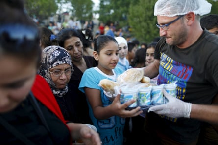 A girl receives donated food from a man as people queue behind her. 