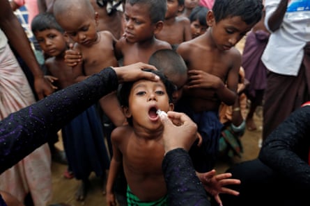 A child receives an oral vaccine in front of  a group of other children