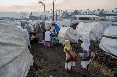 Girls wearing headscarves walk between white tents.