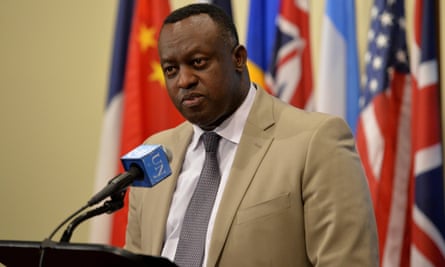 Gasana speaking into a microphone with various countries’ flags behind him