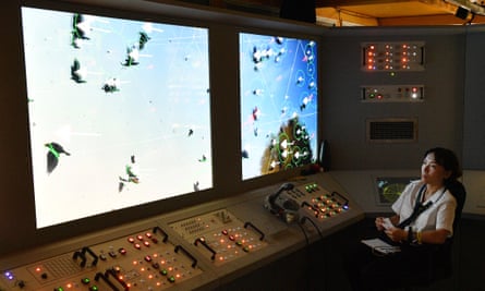 A woman in front of lots of buttons looks at screens with birds flying across.
