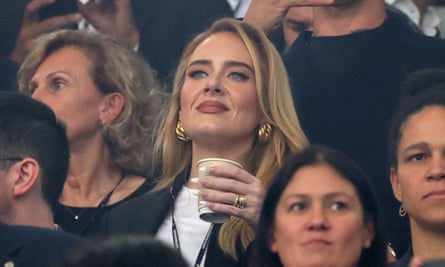 Adele watches the Euro football match wearing a black blazer and white t shirt with gold earrings. 