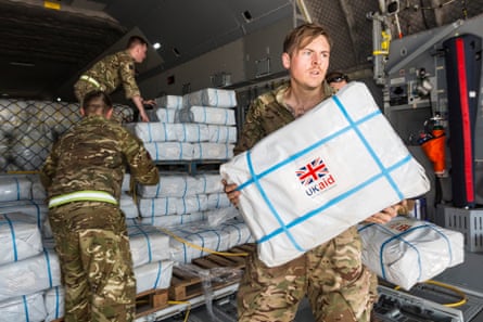 People wearing military fatigues lift white rectangular parcels stamped with a British flag and the words UK Aid.