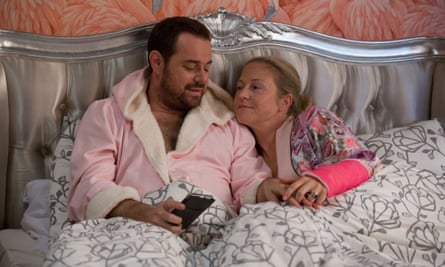 Danny Dyer sitting up in bed wearing a pink dressing gown, with Kellie Bright, in EastEnders.