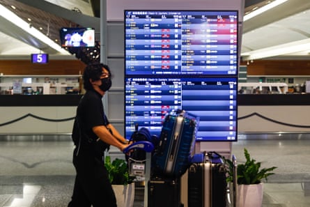 A passenger with suitcases walks past a flight board at Taoyuan international airport, with flights marked as cancelled, as super typhoon Gaemi disrupts international and domestic flights