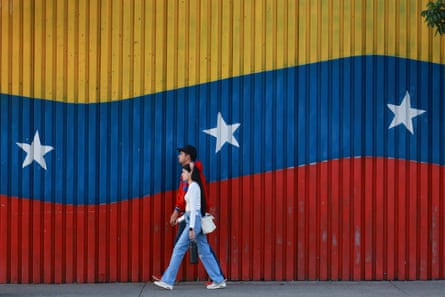 A man and a woman walk in front of a wall painted in the colours of the Venezuelan national flag