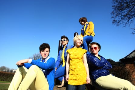 Laura Marling wearing a yellow dress, pictured outside against a blue sky, with members of Noah and the Whale, who are all wearing blue tops and yellow trousers