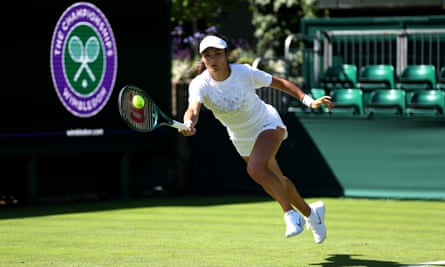 Emma Raducanu, in shorts, T-shirt, visor and big-beaded bracelet over her wristband, purses her lips as she lunges for the ball with her racket