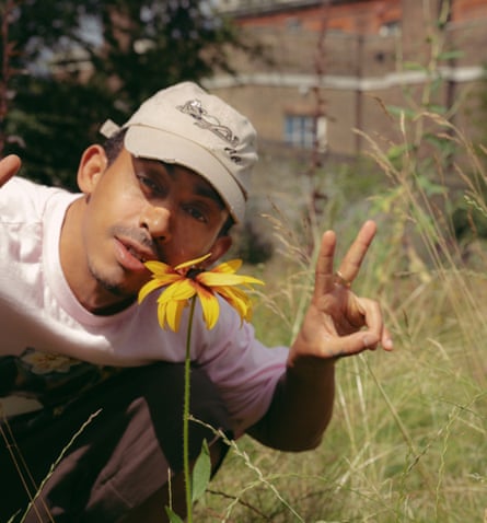 Jordan Stephens making a peace sign behind a flower in Greenwich Park