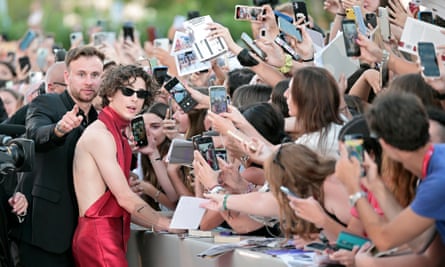 Timothée Chalamet wears dark glass and crimson halter-neck and trouser ensemble