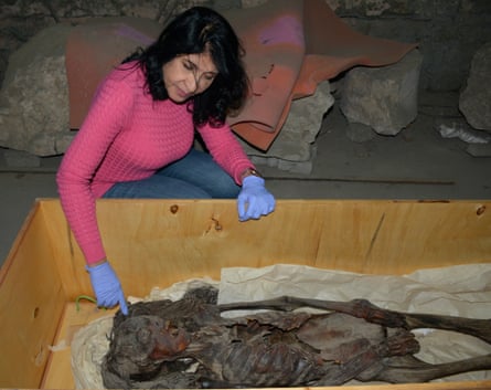 Woman in pink top and blue surgical gloves examines mummy