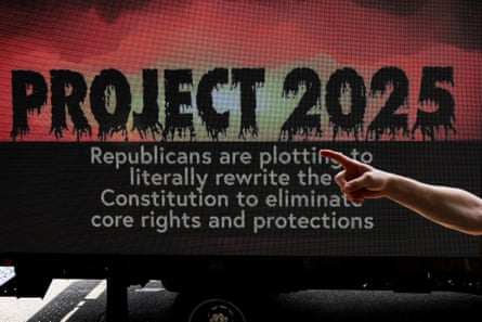 A person gestures in front of a sign saying ‘Project 2025: Republicans are plotting to literally rewrite the constitution to eliminate core rights and protections’