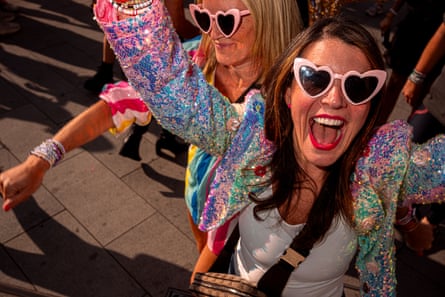 Two women in colourful jackets and heart-shaped sunglasses reach towards the camera