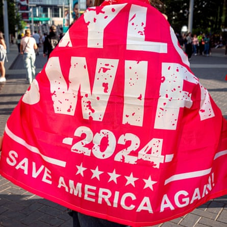 A concertgoer seen from behind wrapped in a large red and white flag that reads ‘Taylor Swift 2024: Save America Again’