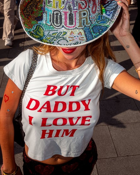 A concertgoer with her face obscured by a sequined cowboy hat reading ‘Eras tour’. Her white T-shirt reads ‘BUT DADDY I LOVE HIM’ in red