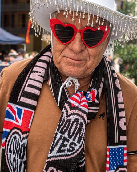 A man in a white beaded cowboy hat, red heart sunglasses, and a scarf commemorating the London Eras tour dates