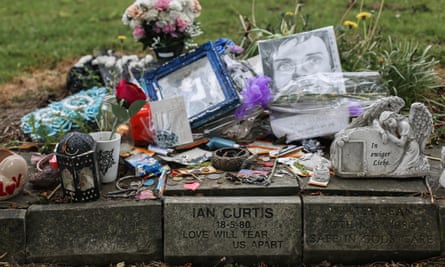 Tributes including flowers and pictures left on top of a small stone monument on which is written: Ian Curtis, 18-5-80, Love Will Tear Us Apart