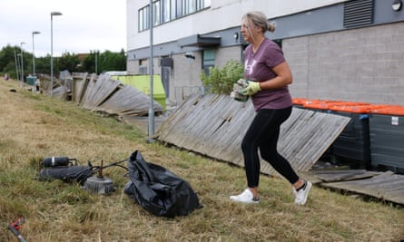 A woman carries bricks away from a building towards a pile of other rubbish