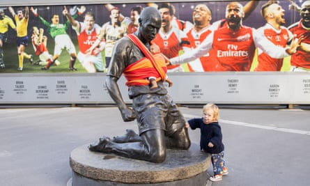 A young child touches the statue of Thierry Henry with a model baby wrapped around in a sling