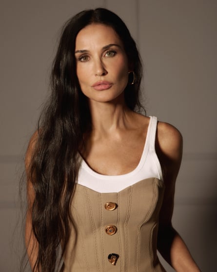 Portrait of Demi Moore with long dark hair and wearing a white T-shirt and beige corset