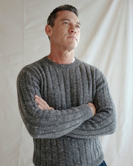 ‘The only thing I could talk about to people I knew was the religion.’ Portrait of Luke Evans with his arms crossed wearing a grey knit.