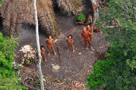 An aerial photograph of Indigenous people standing in a clearing holding long bows, spears and machetes and looking upwards.