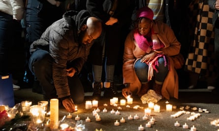 A man and a woman kneel down to light candles on the ground