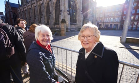 Two older women stand by a barrier outside the Minster, smiling at the camera