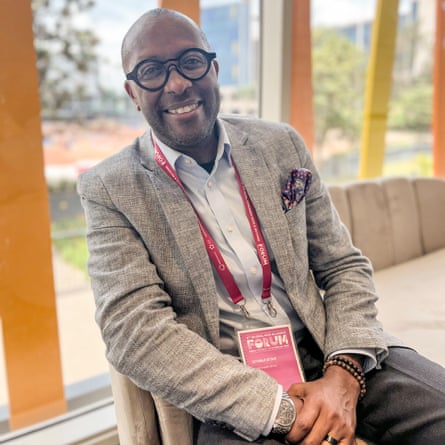 A smiling man in blazer and glasses sitting down