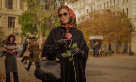 a woman in a silk headscarf and black coat holding a pink rose