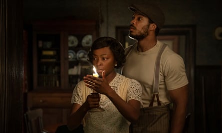 a woman holds a candle and a man looks up behind her