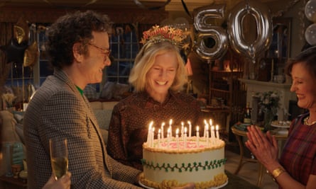 a man holds a big birthday cake as a woman smiles over it