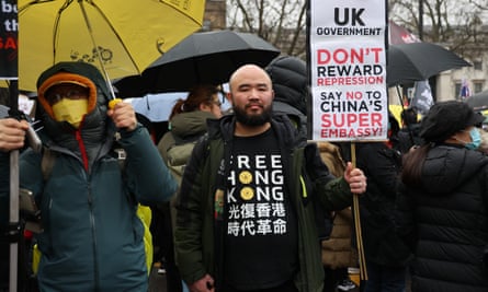 Protesters under umbrellas, including a man centre-frame in a T-shirt that reads Free Hong Kong, holding a placard that reads ‘UK government: don’t reward repression; say no to China’s super embassy’