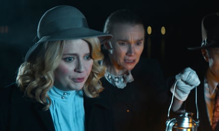 Mischa Barton wearing period clothing holding a lamp and looking in horror at something in Invitation to Murder. 